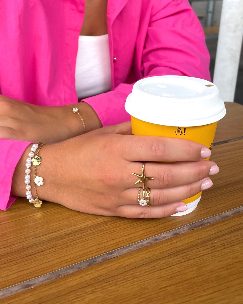 Goudkleurige ringen om vingers van vrouw die een koffie beker vast heeft.