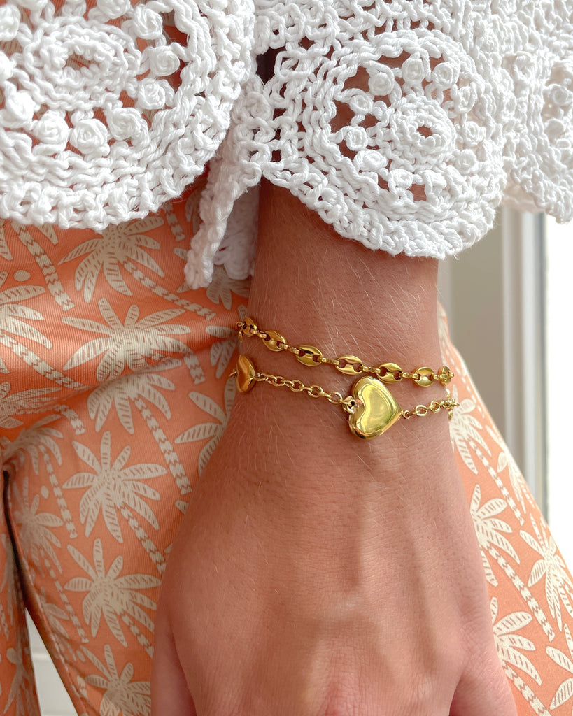 Pols van vrouw met goudkleurige schakelarmband en gouden armband met hartjes.