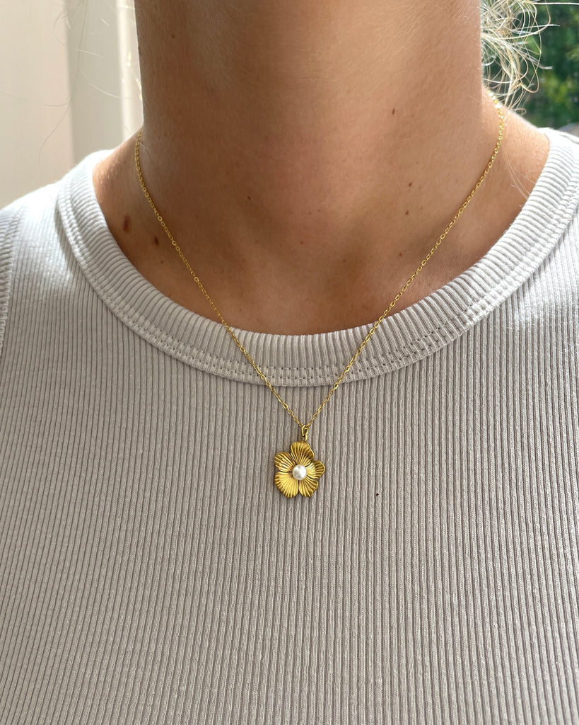 goudkleurige ketting met bloemetjes bedel en pareltje om hals van vrouw.