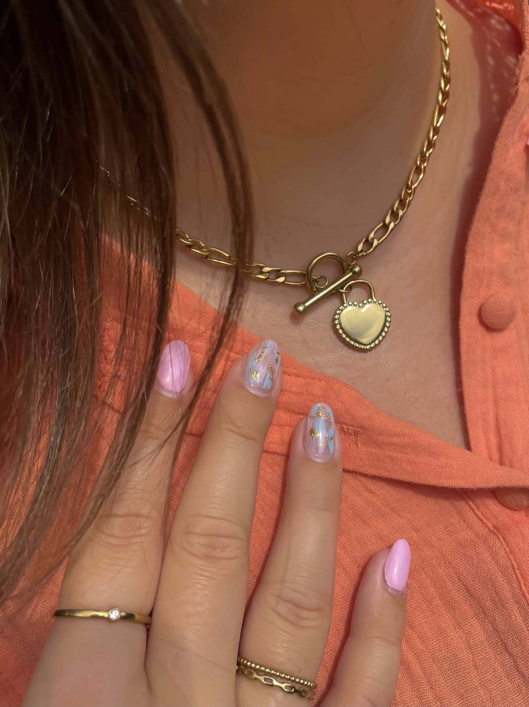 vrouw met een gouden Stainless steel ketting met een hartjes bedel om de hals en gouden ringen om de vingers